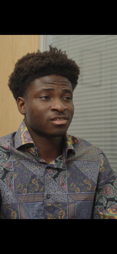 Kevin Golding Young man wearing a patterned shirt, looking thoughtfully to the side.