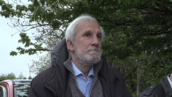 Steven Grant Elderly man with grey hair, wearing a coat, looking contemplatively outdoors.
