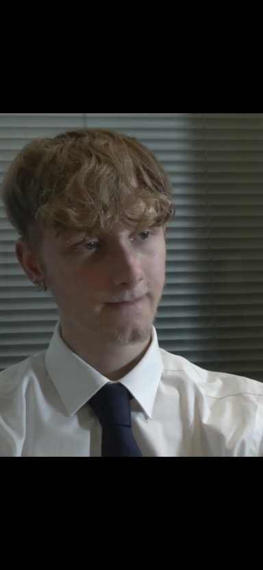 Jason Blake Young man with curly hair, wearing a white shirt and dark tie, appears thoughtful.