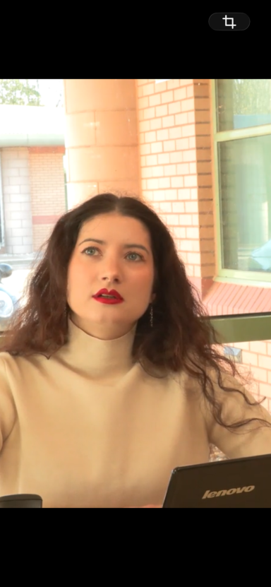 Samantha Hayes Young woman with long, curly hair, wearing a white turtleneck, looking thoughtfully upward.