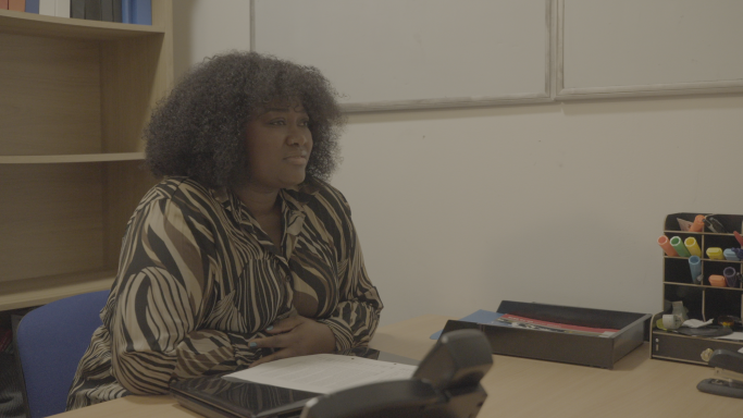 Amy Young A woman with curly hair sits at a desk, engaged in conversation.
